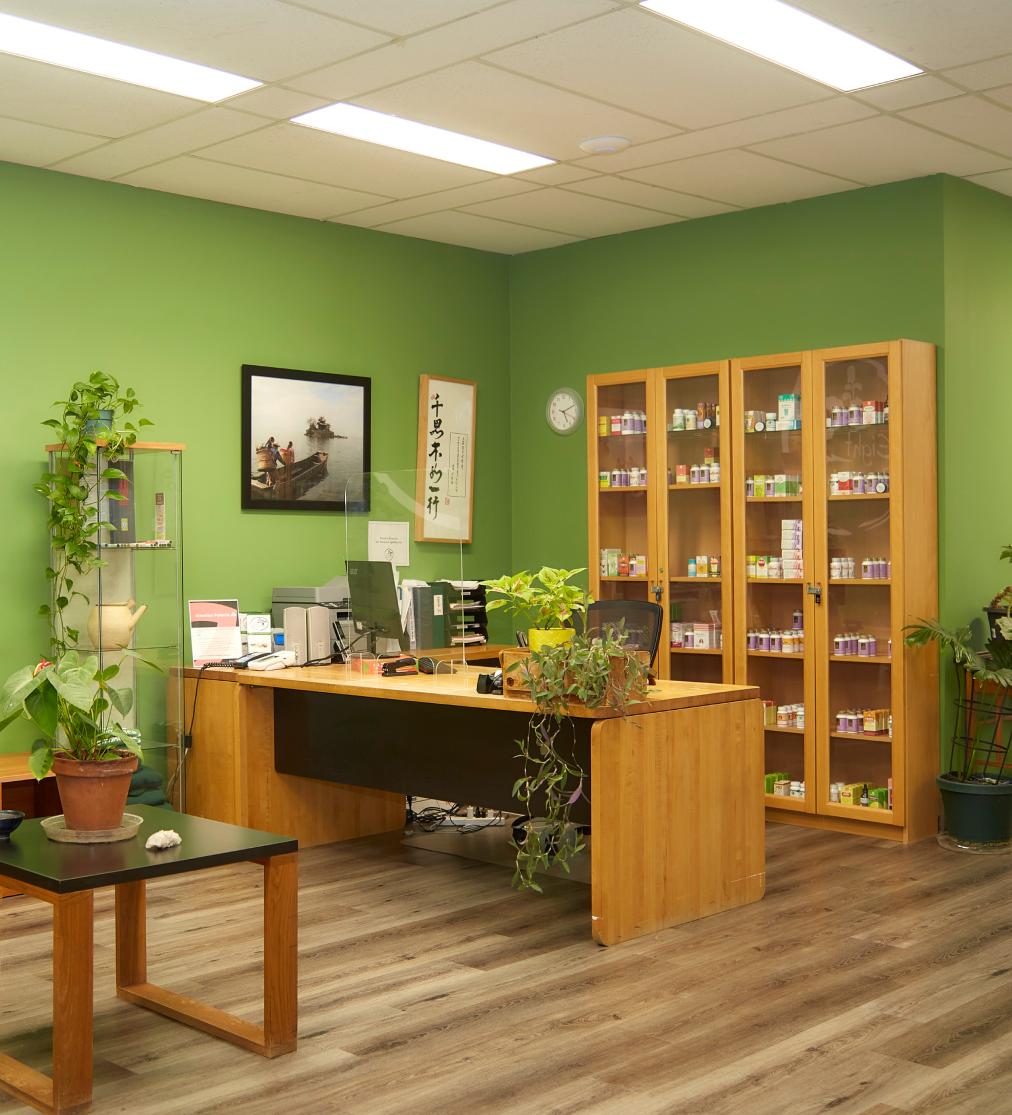 Image of an office within our school. A wooden table is pictured against a green wall backdrop, surrounded by decorative plants.